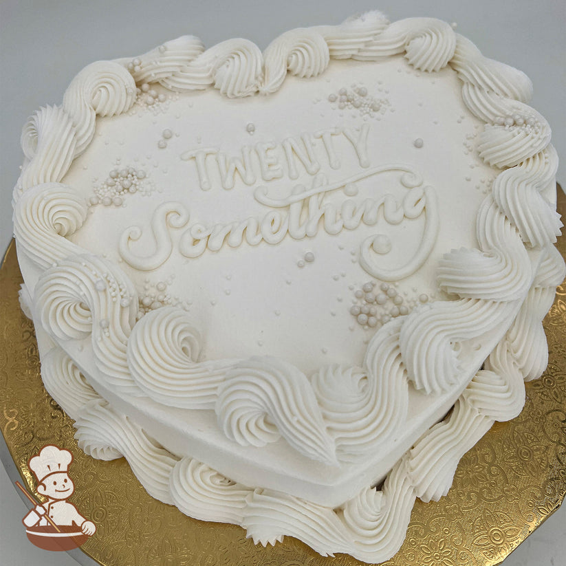 Heart-shaped white cake, wavy trim with pearl clusters, sugar pearls scattered on top, gold base.