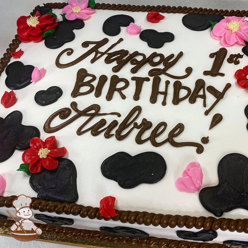 Sheet cake with white frosting, black cow print spots, red and pink apple blossom decorations, and a brown rope trim border.