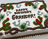 Sheet cake with white frosting, decorated with green buttercream cacti with red flowers, gray horseshoes, brown rope trim, and plastic green grass accents.