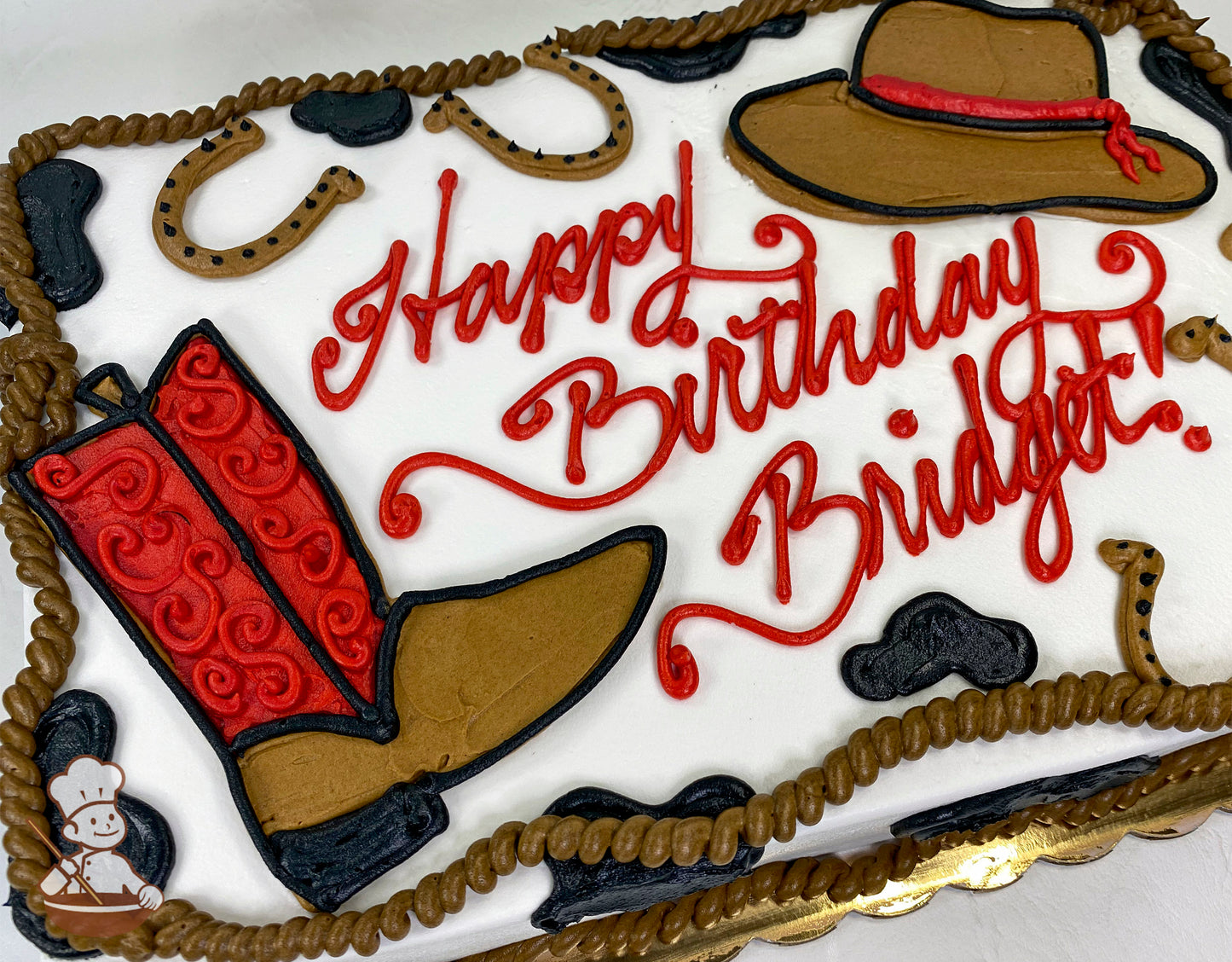 Sheet cake with buttercream decorations of a red cowboy boot, brown cowboy hat with a red band, horseshoes, black cow spots, and a rope border.
