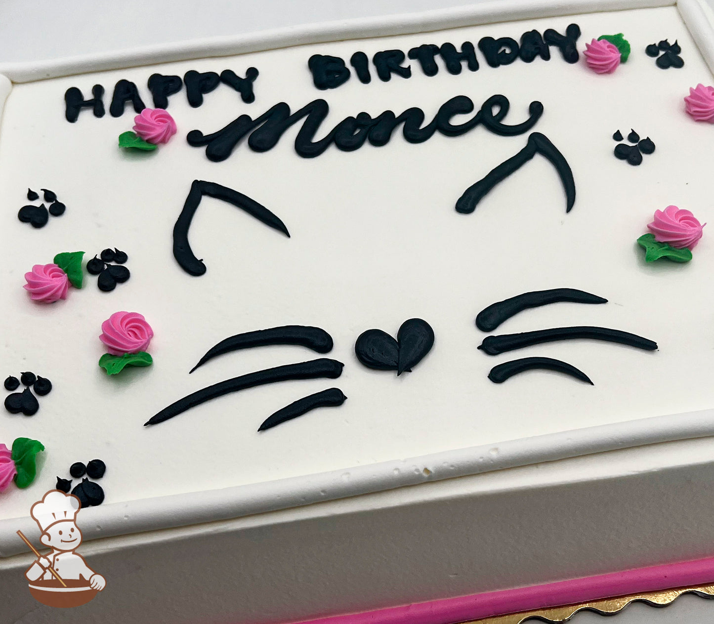 White sheet cake with black buttercream cat face design, including ears, whiskers, and a heart-shaped nose. Decorated with pink buttercream roses and black paw prints.