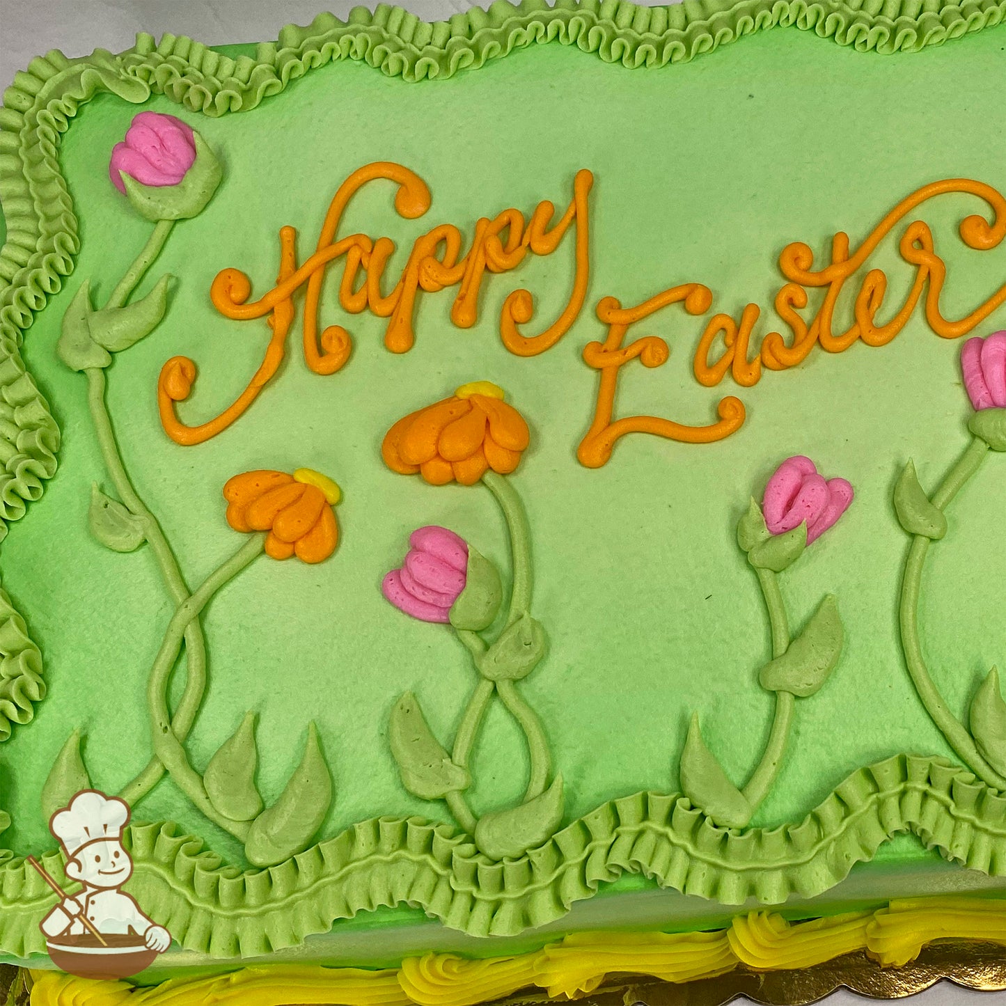 Sheet cake with green frosting, orange and pink buttercream flowers, green stems and leaves, and ruffled green borders.