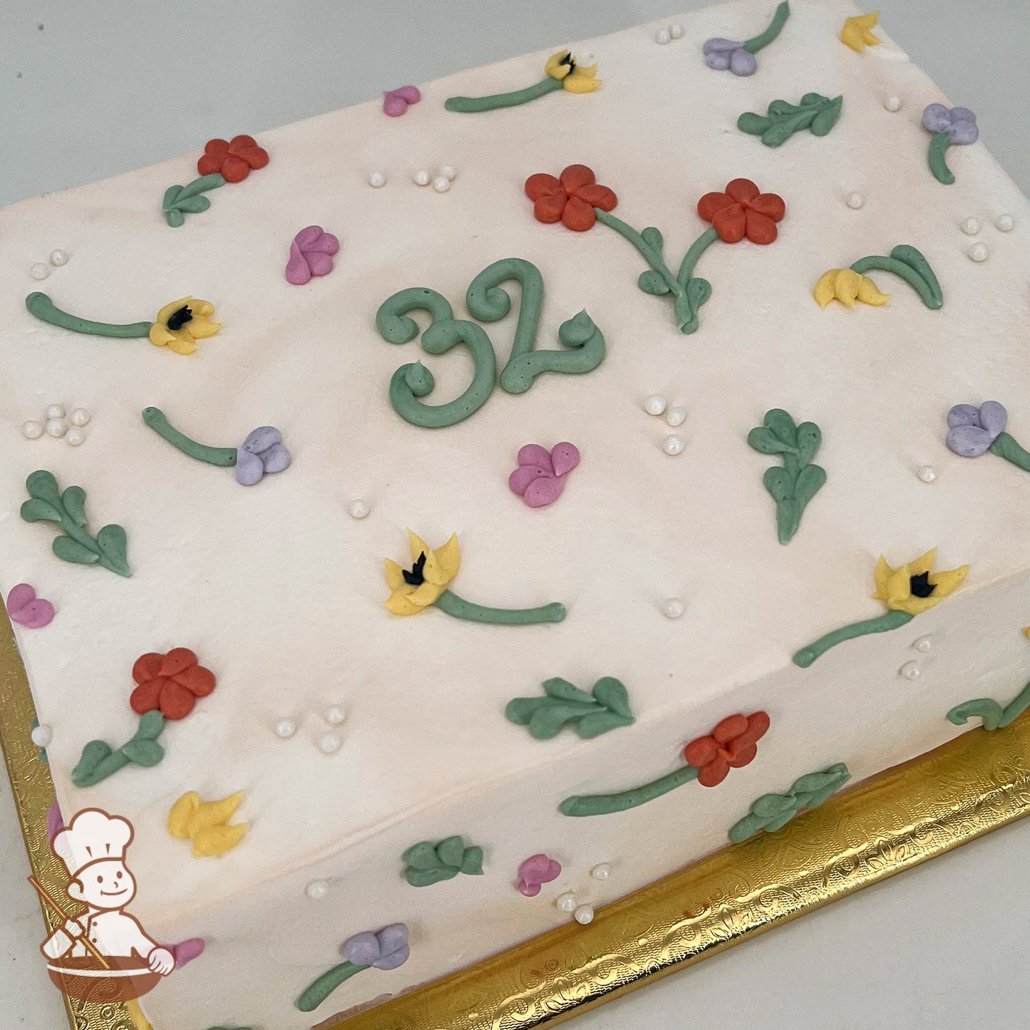 A rectangular sheet cake decorated with colorful buttercream flowers, green stems, and scattered white sugar pearl beads.