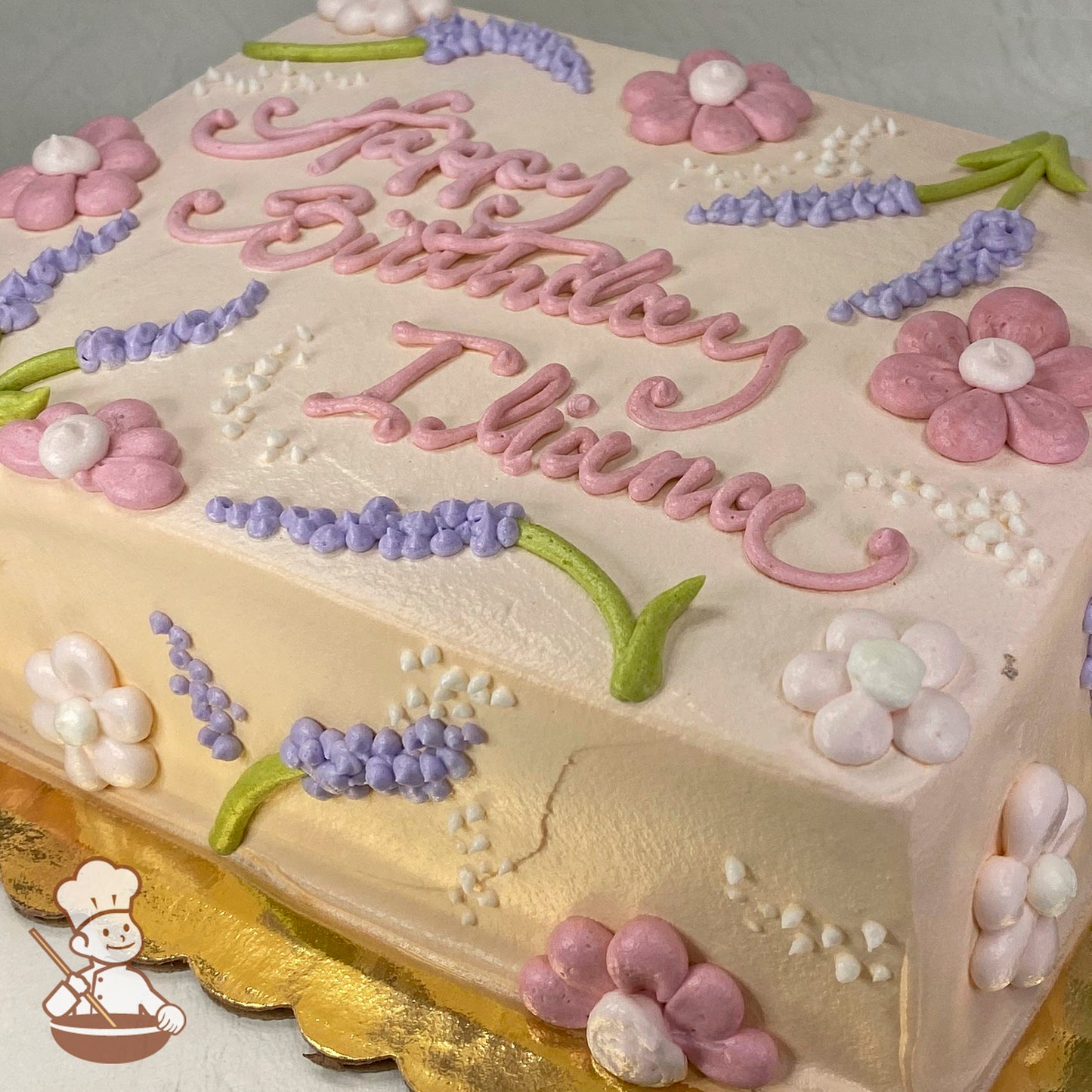 Sheet cake with pink and purple buttercream flowers, including daisies and lavender, on a light cream background.