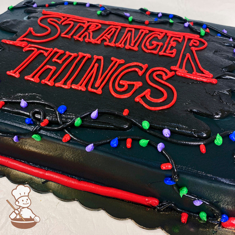 Black sheet cake with red buttercream lettering, surrounded by colorful buttercream Christmas lights in red, green, blue, and purple, on black icing strands.