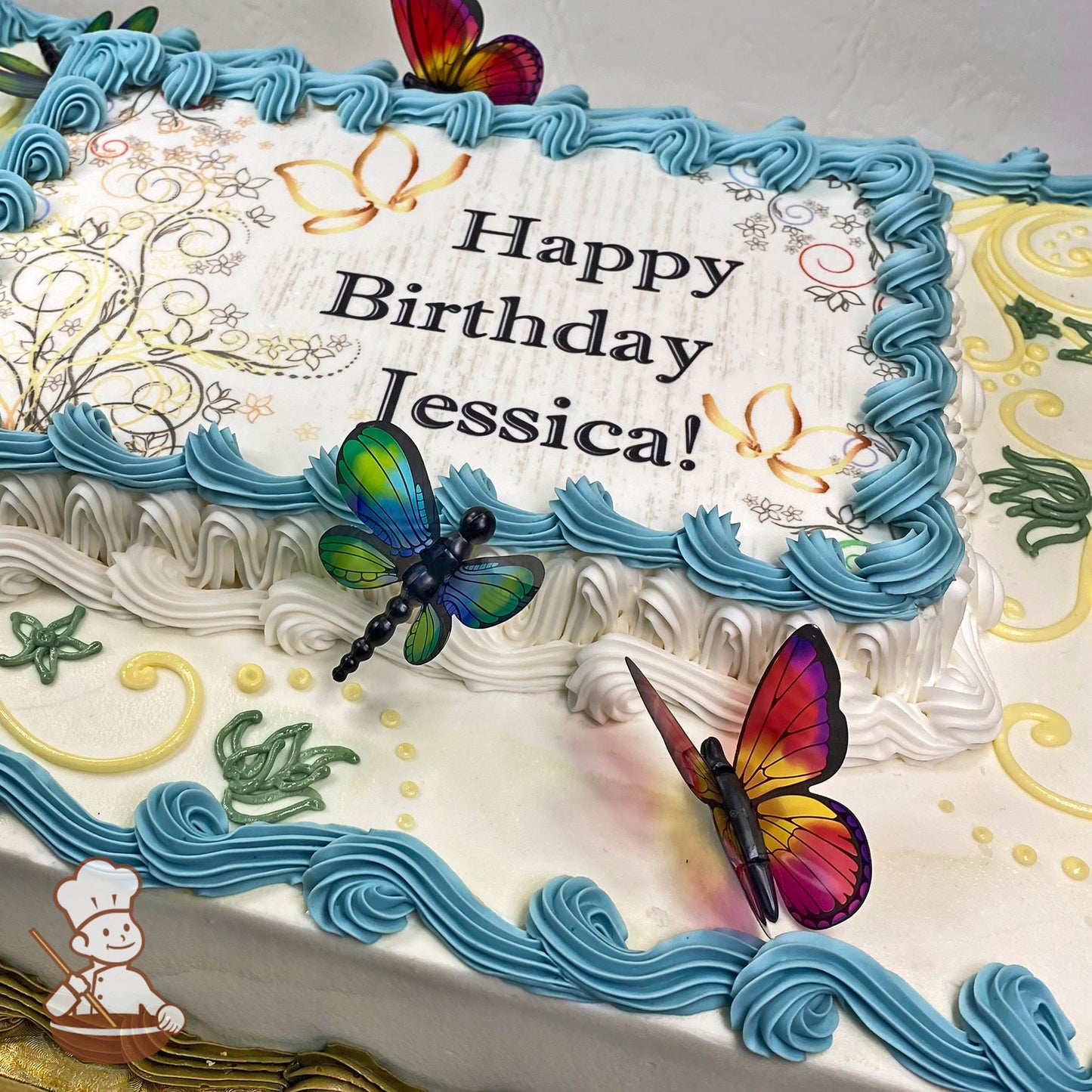 Sheet cake with blue and white buttercream borders, plastic dragonflies and butterflies, scroll designs, and floral buttercream accents.