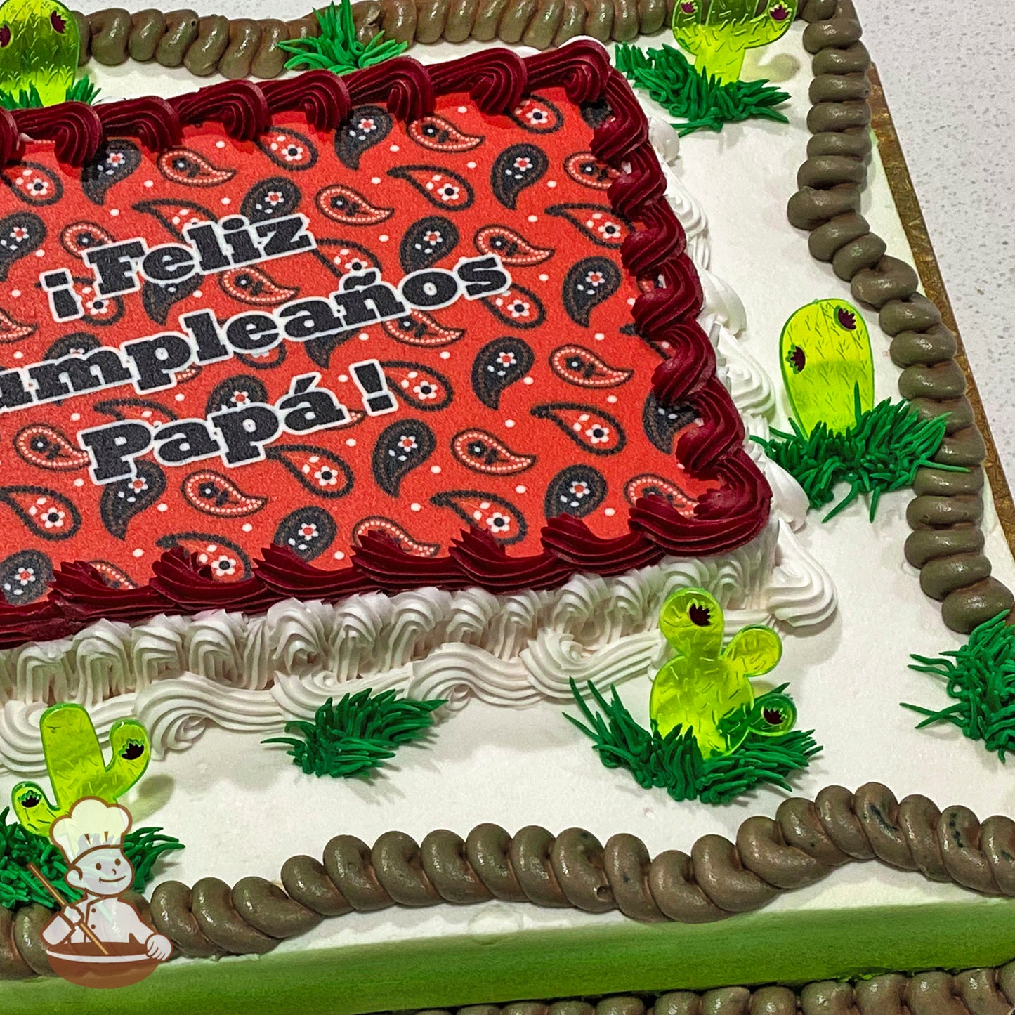 Sheet cake with buttercream decorations, featuring plastic cactus picks, green grass accents, and a brown rope-like trim around the edges.