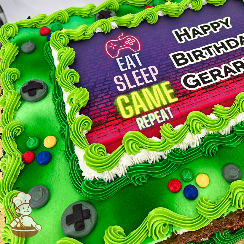 Sheet cake with green frosting, swirled borders, and gamer-themed decorations, including controller buttons and colorful round accents.