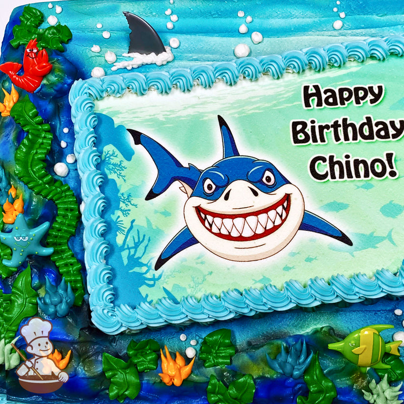 Sheet cake with an ocean theme, featuring hand-piped seaweed, plants, bubbles, and ocean spray. Plastic starfish, lobster, and shark fin decorations are included.