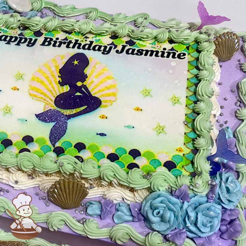Sheet cake with green buttercream swirl trims, blue roses, and plastic seashells and mermaid tails.