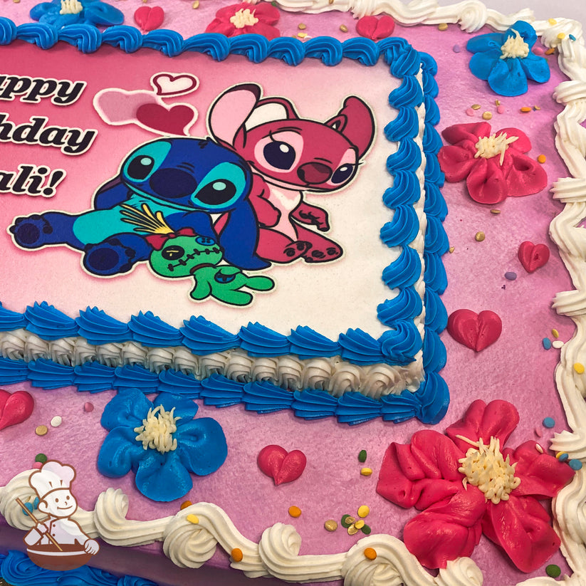 Sheet cake with pink frosting, blue and white piped borders, pink and blue buttercream flowers, small pink hearts, and colorful sprinkles.