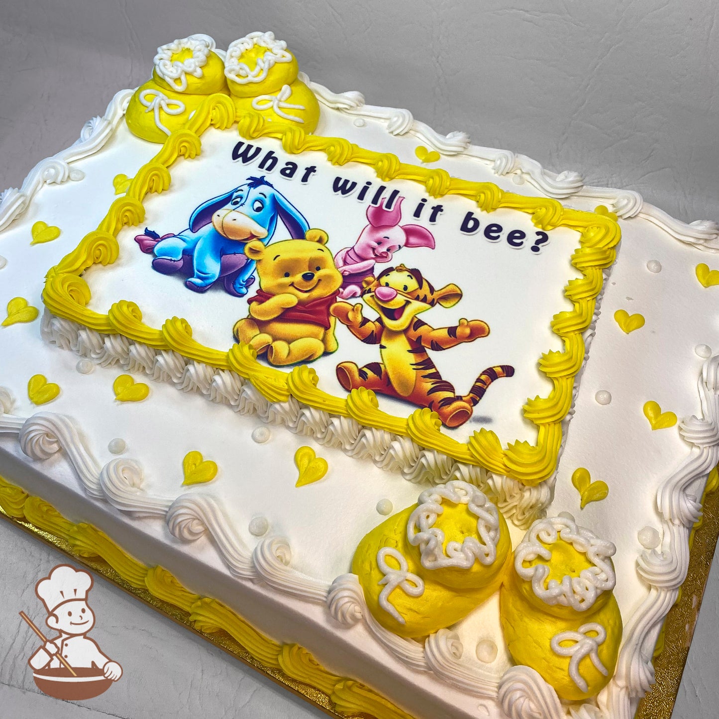Sheet cake with white frosting, yellow piped borders, small yellow hearts, and baby bootie decorations with white laces.