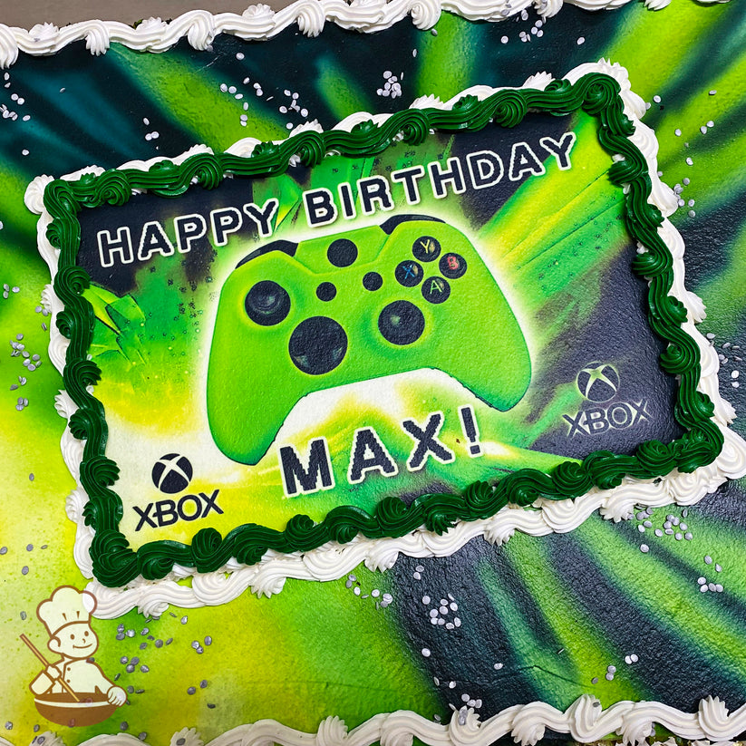 Sheet cake with green and black spray design, bordered by white and green buttercream swirl trims, silver confetti sprinkles scattered on top.