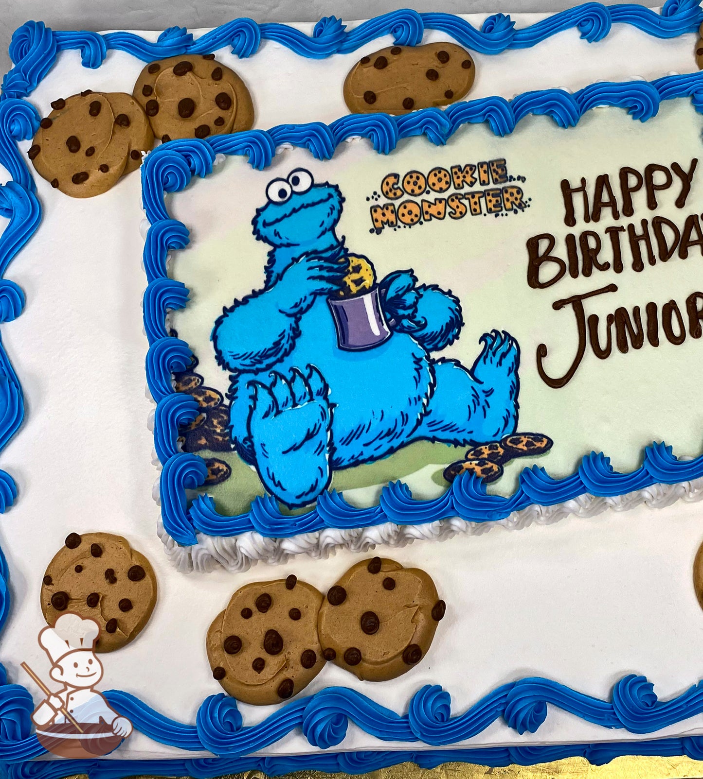 Sheet cake with blue buttercream swirl trims along the edges, decorated with chocolate chip cookie designs and a printed image in the center.