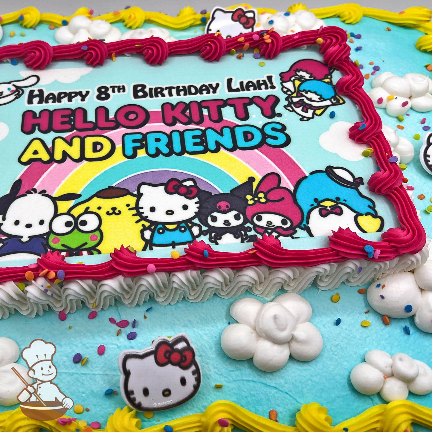 Sheet cake with blue frosting, hand-piped white clouds, pink and yellow borders, Hello Kitty plastic rings, and colorful sprinkles.