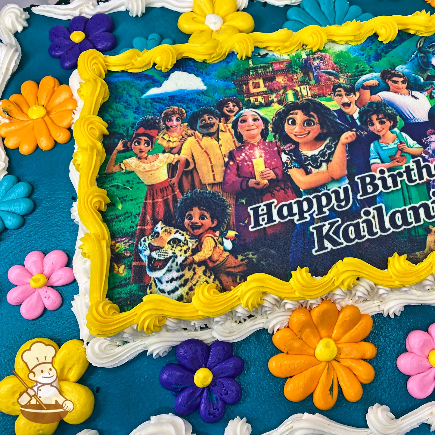 Sheet cake with colorful buttercream daisy flowers, including yellow, orange, pink, blue, and purple daisies, surrounding a printed photo layer.