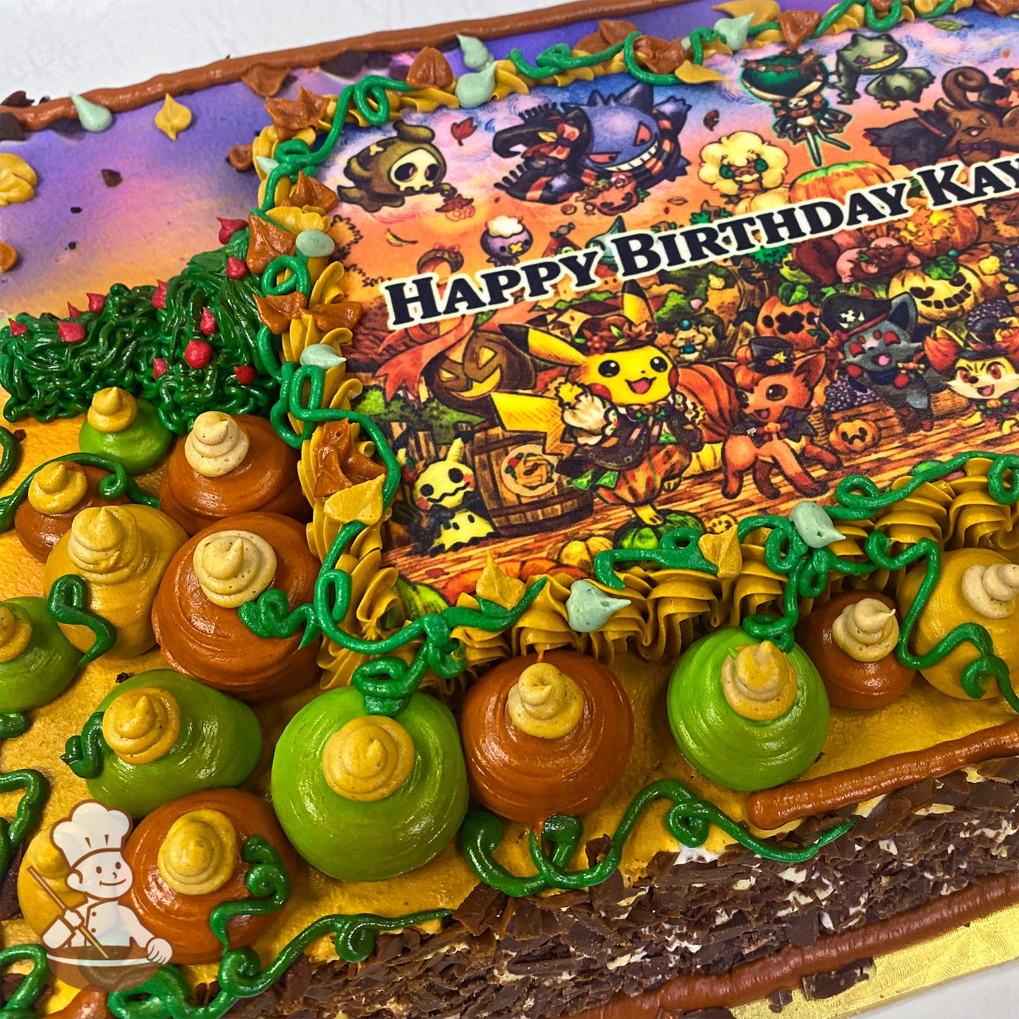 Sheet cake with colorful buttercream pumpkins, green vines, and autumn leaves surrounding a printed image.
