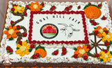 Sheet cake with buttercream decorations, featuring orange and yellow flowers, red swirls, and orange pumpkins. A brown wheel design is also present.