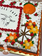 Sheet cake with buttercream decorations, featuring orange and yellow flowers, red swirls, and orange pumpkins. A brown wheel design is also present.