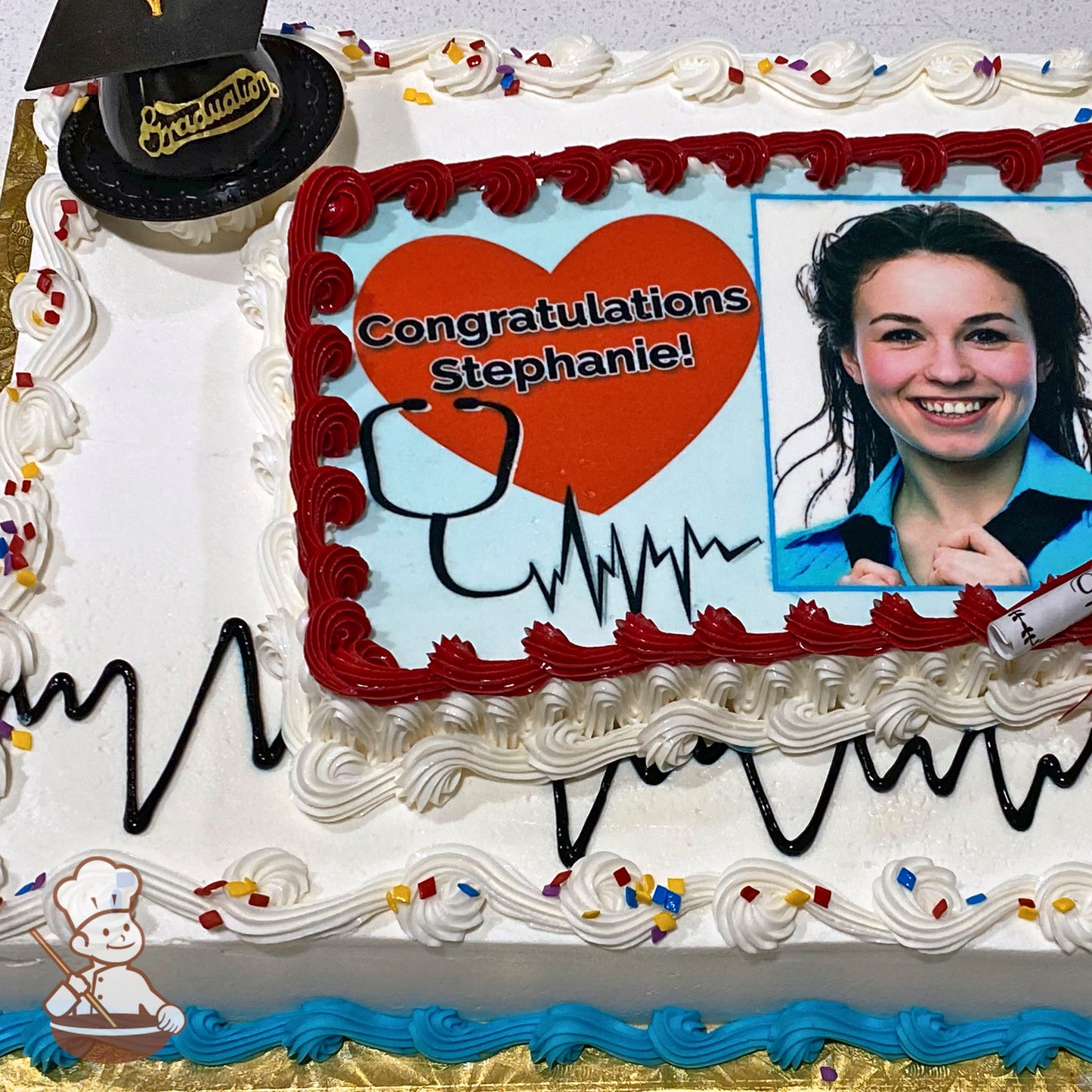 Sheet cake with white icing, red and blue piped borders, black heartbeat design, colorful sprinkles, and a plastic graduation cap decoration.