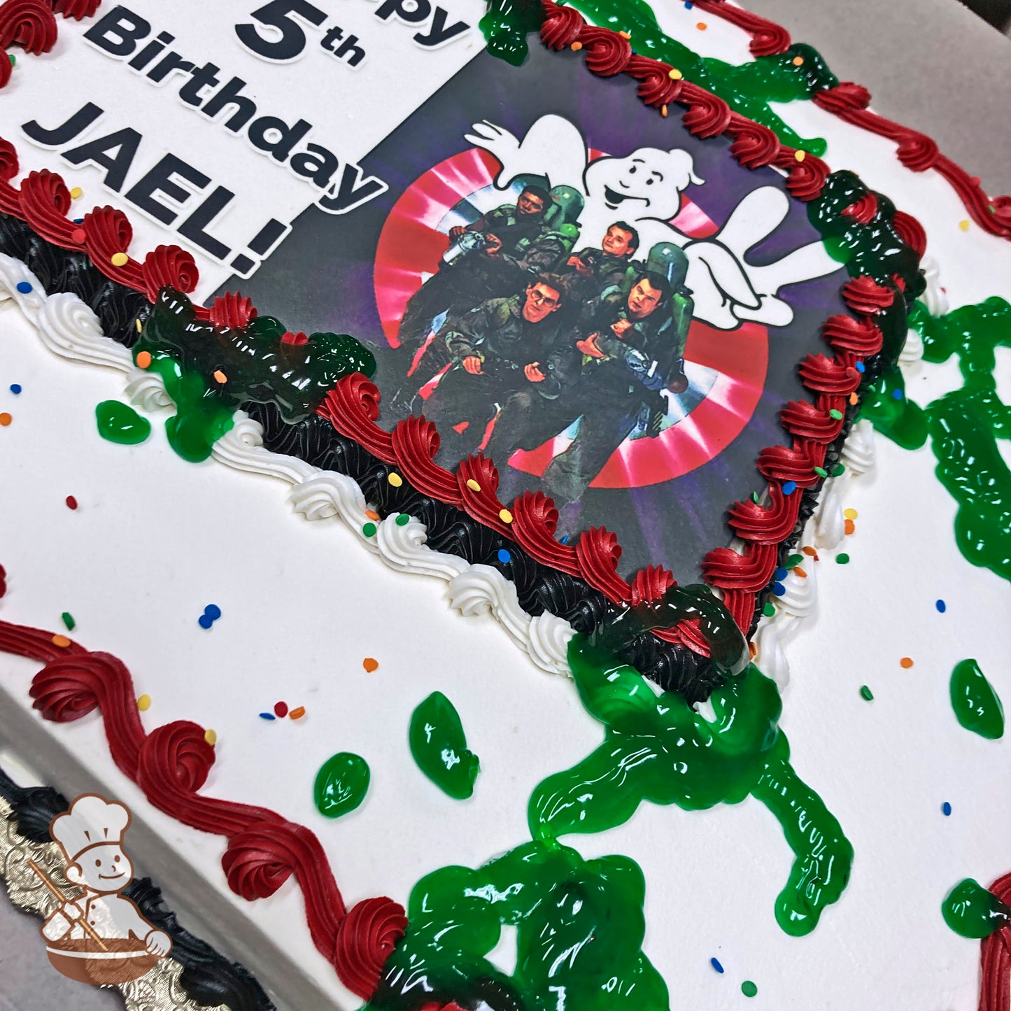 Sheet cake with white frosting, red and black piped borders, green slime decorations, and scattered colorful sprinkles.
