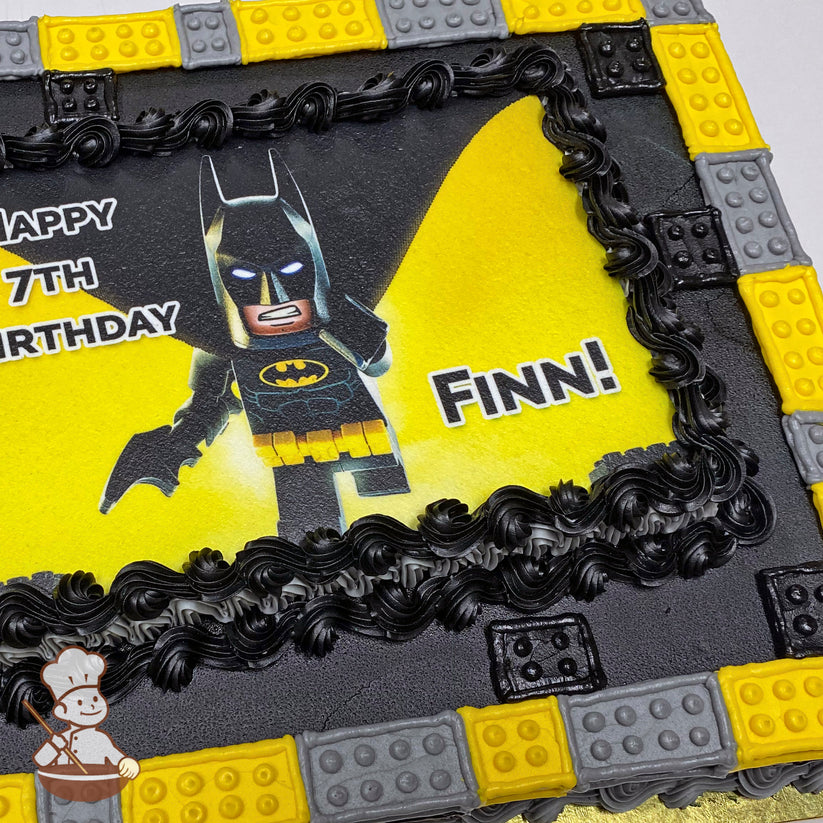 Sheet cake with black buttercream swirl trims, bordered by yellow and gray buttercream bricks resembling Lego blocks.