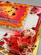 Sheet cake with a printed photo layer framed by orange and white buttercream swirls, decorated with buttercream noodles, red sauce, and meatballs.