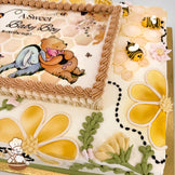 Sheet cake with honeycomb piping, yellow and cream buttercream flowers, buttercream bees, green leaves, and a printed photo layer framed by piped frosting.
