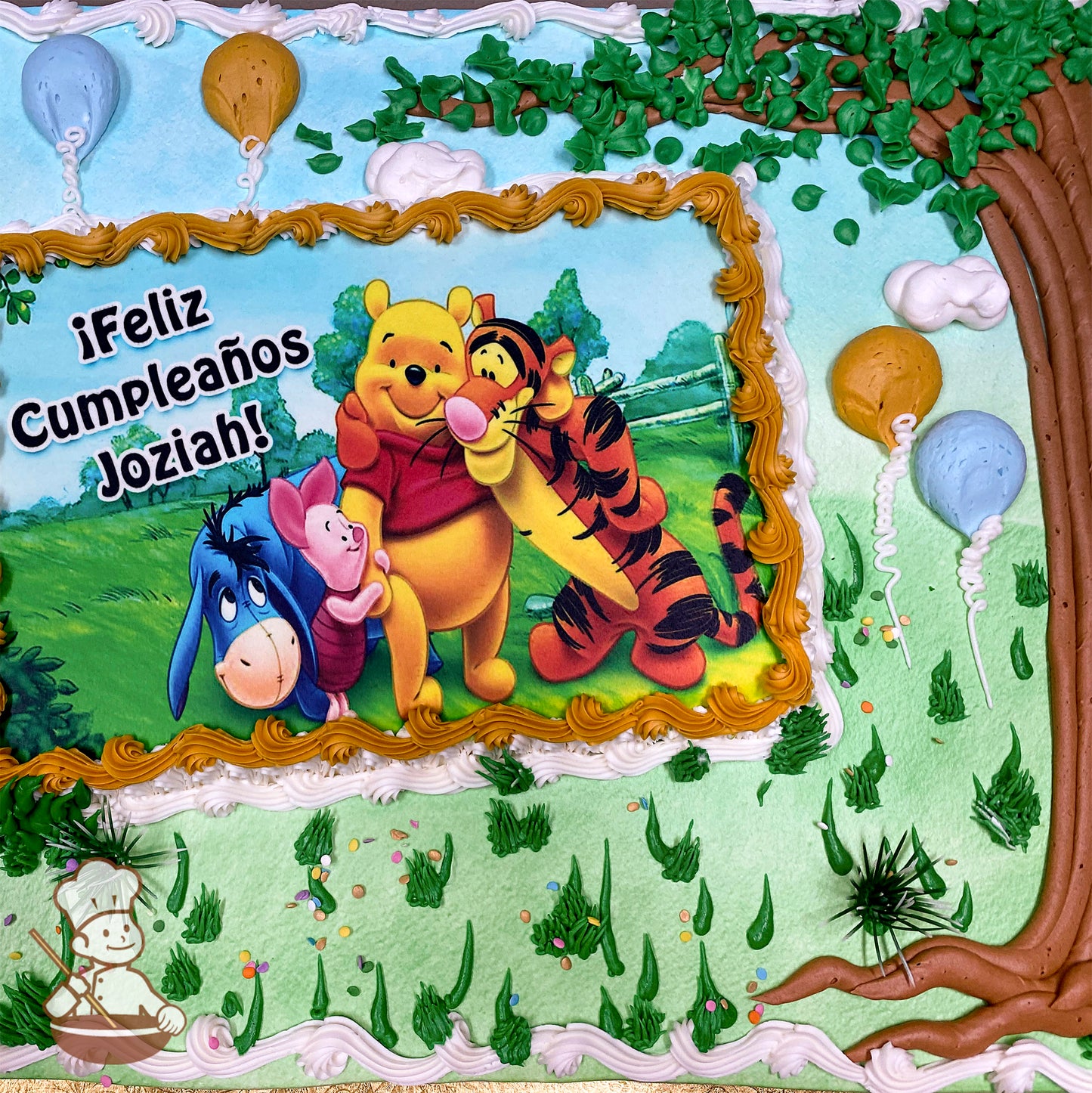 Sheet cake with a printed photo layer framed by yellow buttercream. Decorations include plastic bushes, green buttercream grass, tree design, and balloons.