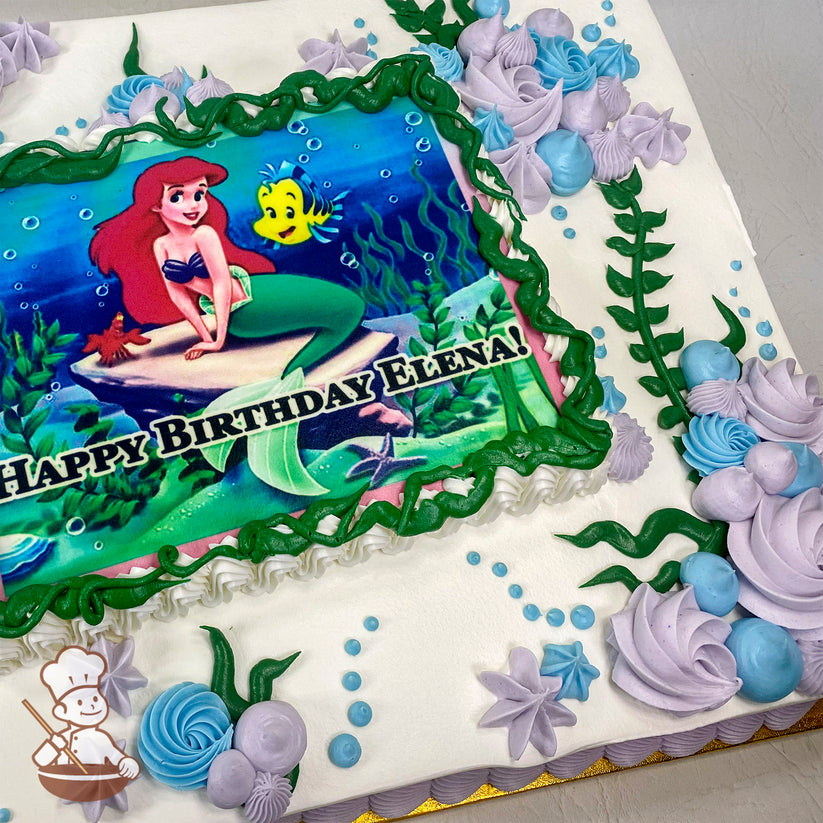 Sheet cake with a printed photo layer framed by green buttercream swirls, decorated with purple and blue buttercream swirls, star shapes, kelp, and bubbles.