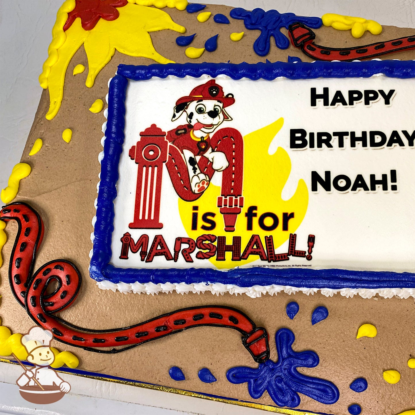 Sheet cake with buttercream decorations, featuring a red fire hose, blue water splashes, yellow flames, and a printed photo layer framed in blue icing.