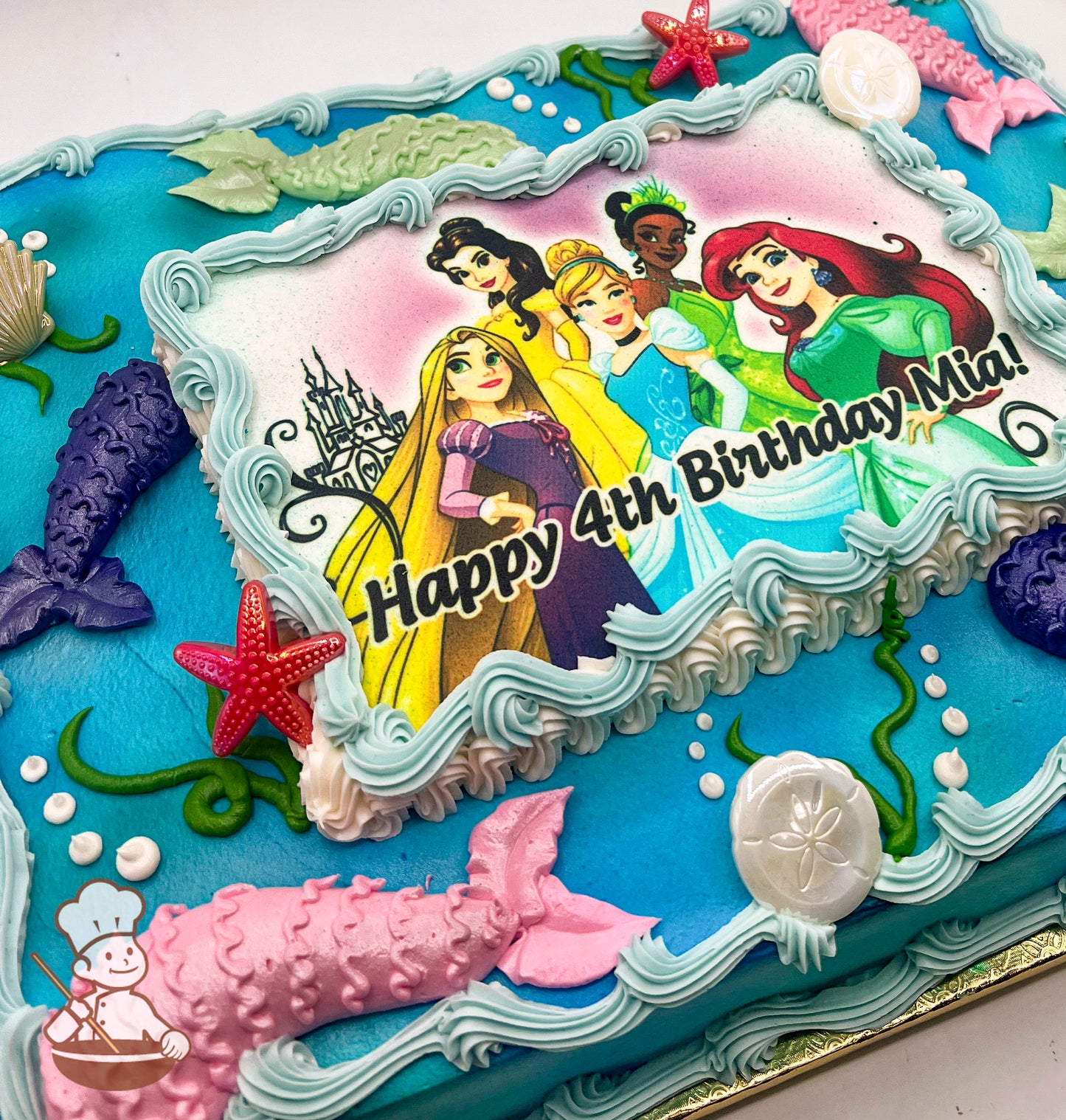 Sheet cake with blue canvas, featuring mermaid tails, seashells, starfish rings, and seaweed decorations around a printed photo layer.