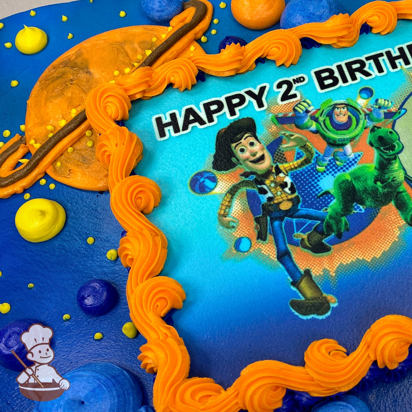 A sheet cake with a blue base and a printed photo layer framed by orange piping. Planet and ring designs decorate the cake.