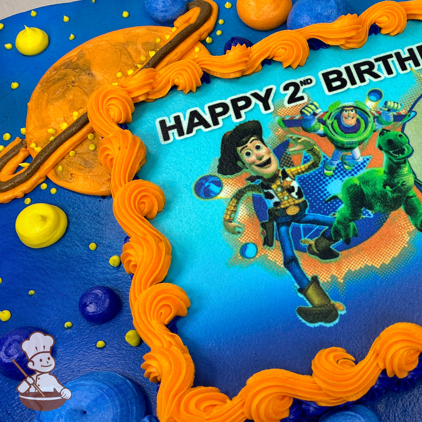 A sheet cake with a blue base and a printed photo layer framed by orange piping. Planet and ring designs decorate the cake.