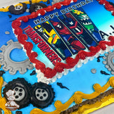 Sheet cake with a blue base, red and yellow piped borders, gray gear decorations, and black piped tires around the edges.