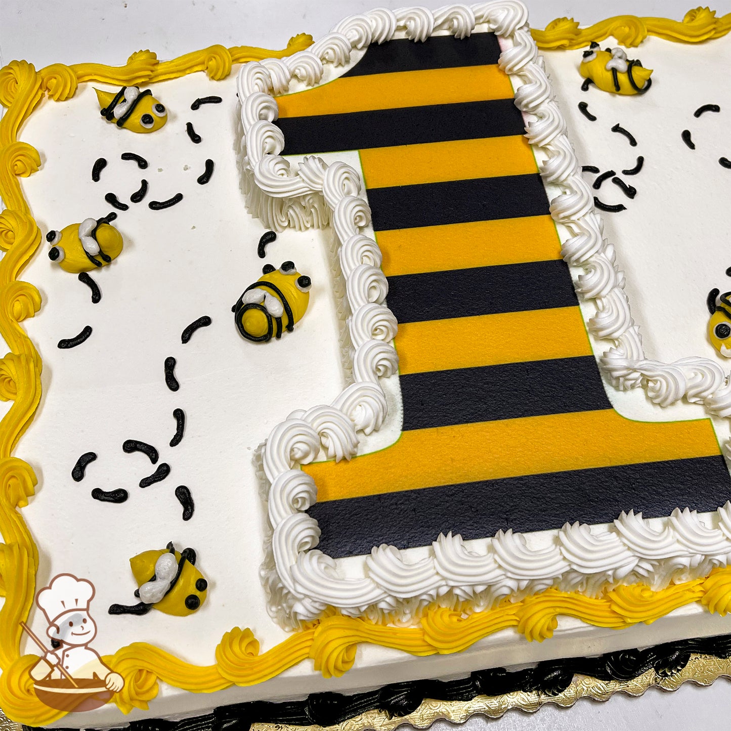 Sheet cake with a large striped number one, surrounded by buttercream bees and trails. Yellow and white icing borders the cake.