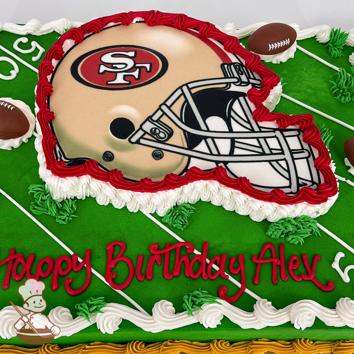 Sheet cake with green frosting resembling a football field, featuring a San Francisco 49ers helmet design outlined in red and white buttercream, with small plastic football decorations.