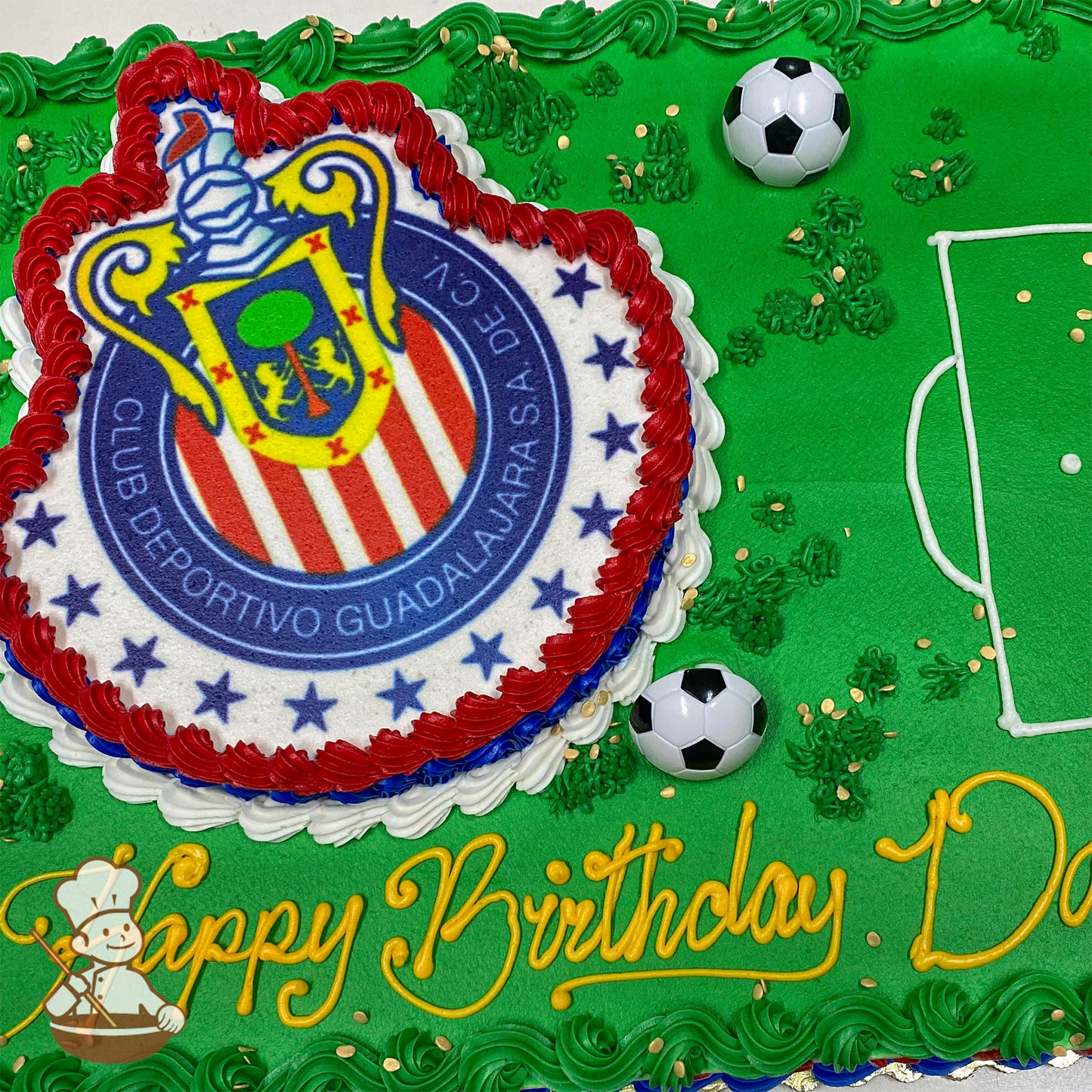Sheet cake with green frosting resembling a soccer field, featuring a Guadalajara Chivas logo cutout bordered in red, white, and blue, plastic soccer balls, and piped grass accents.