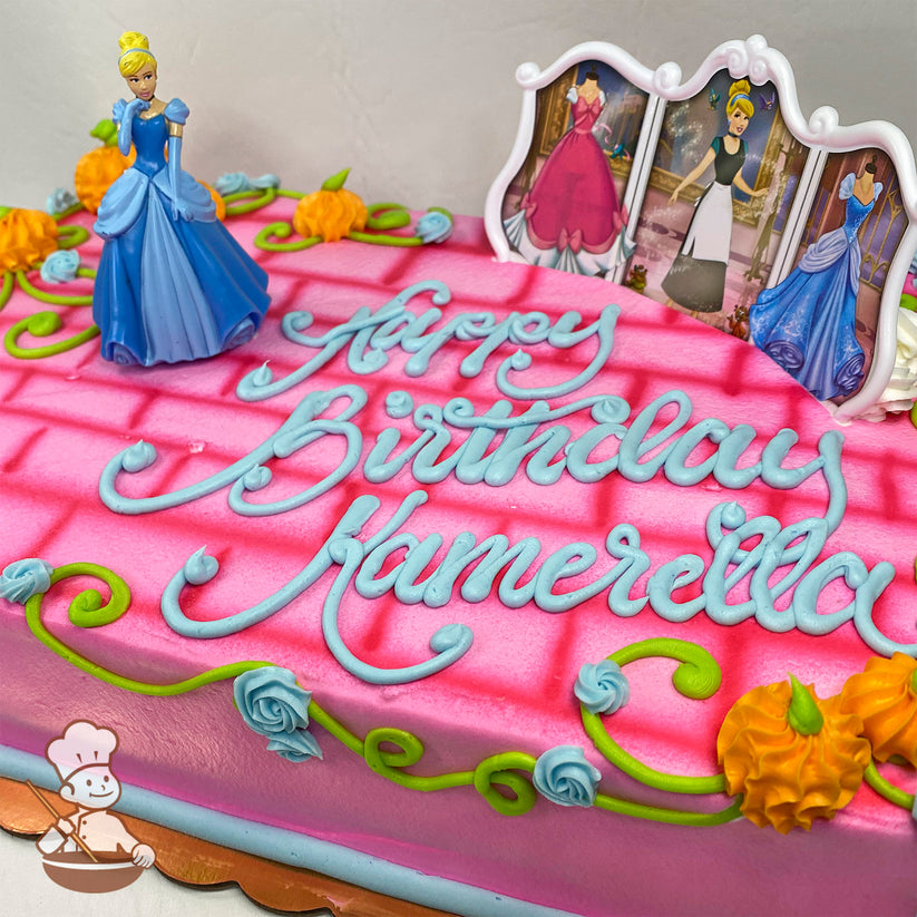 Pink sheet cake with a brick pattern, buttercream vines, blue roses, orange pumpkin decorations, Cinderella figurine, and a frame with Cinderella scenes.