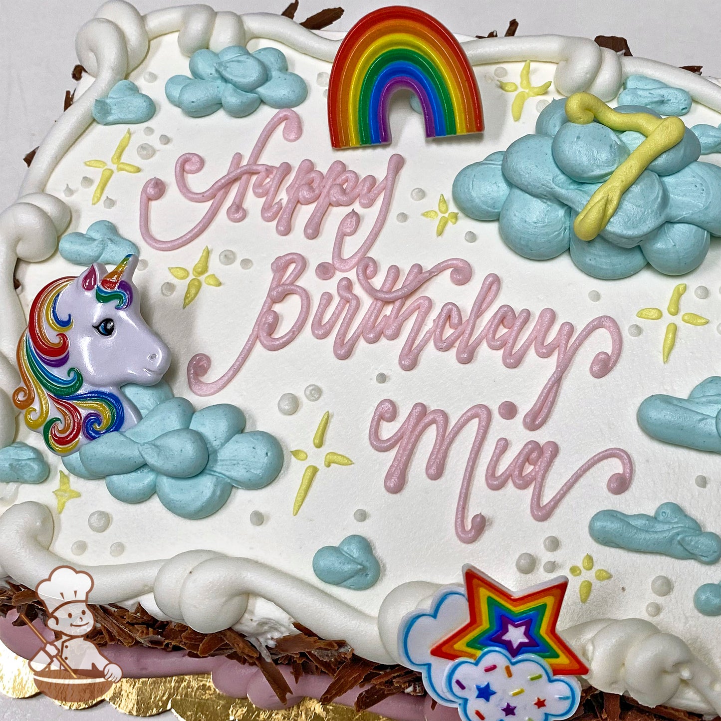 Sheet cake with white frosting, pastel blue buttercream clouds, plastic unicorn and rainbow decorations, and colorful star accents.