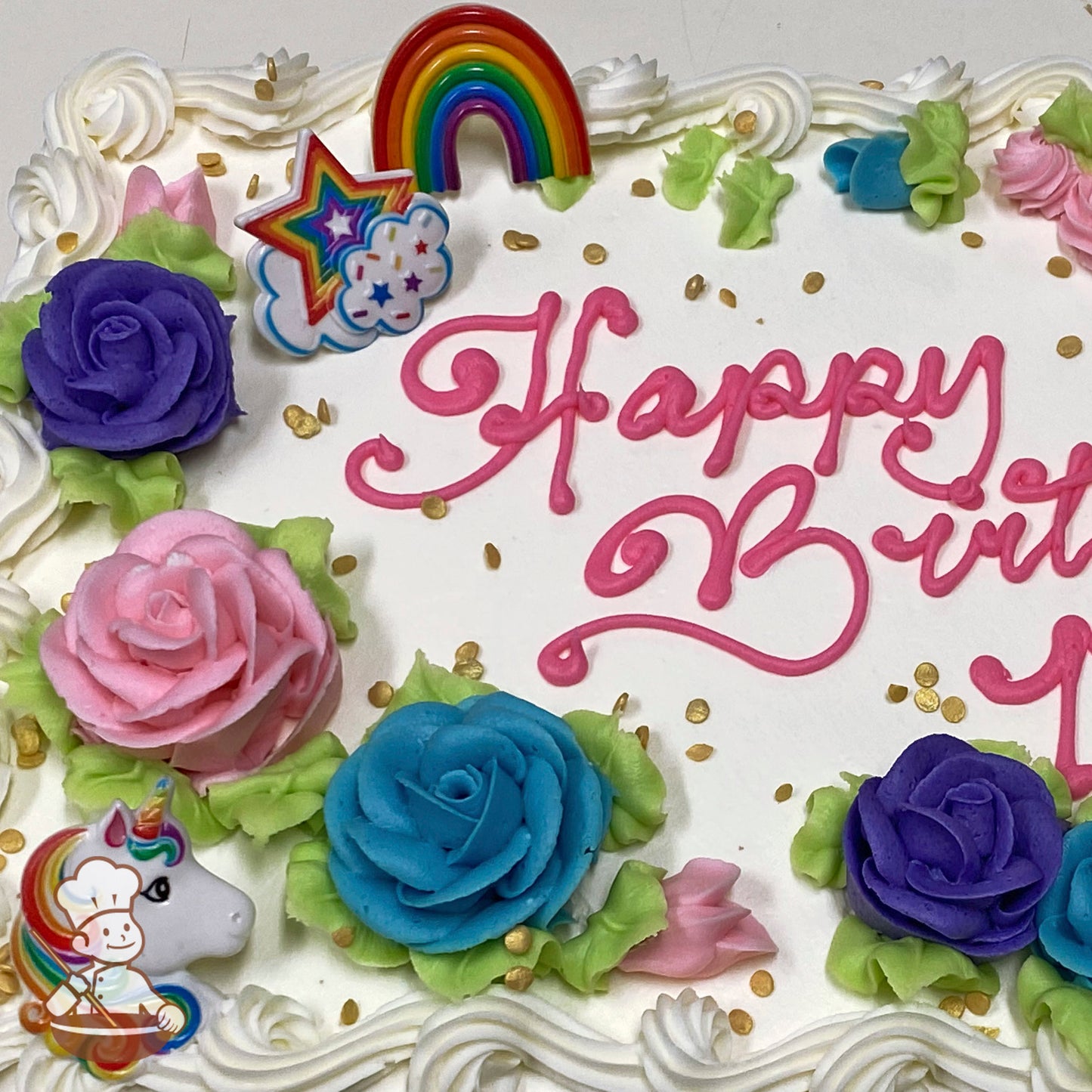 Sheet cake with colorful buttercream roses in pink, blue, and purple, green leaves, a plastic unicorn, rainbow, and star decorations, and gold sprinkles.
