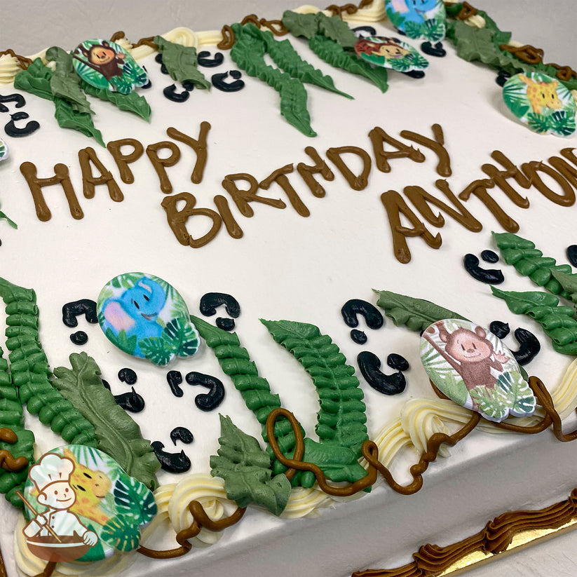 Sheet cake with white frosting, decorated with green buttercream jungle leaves, plastic rings featuring safari animals (elephant, giraffe, monkey), and animal print accents.