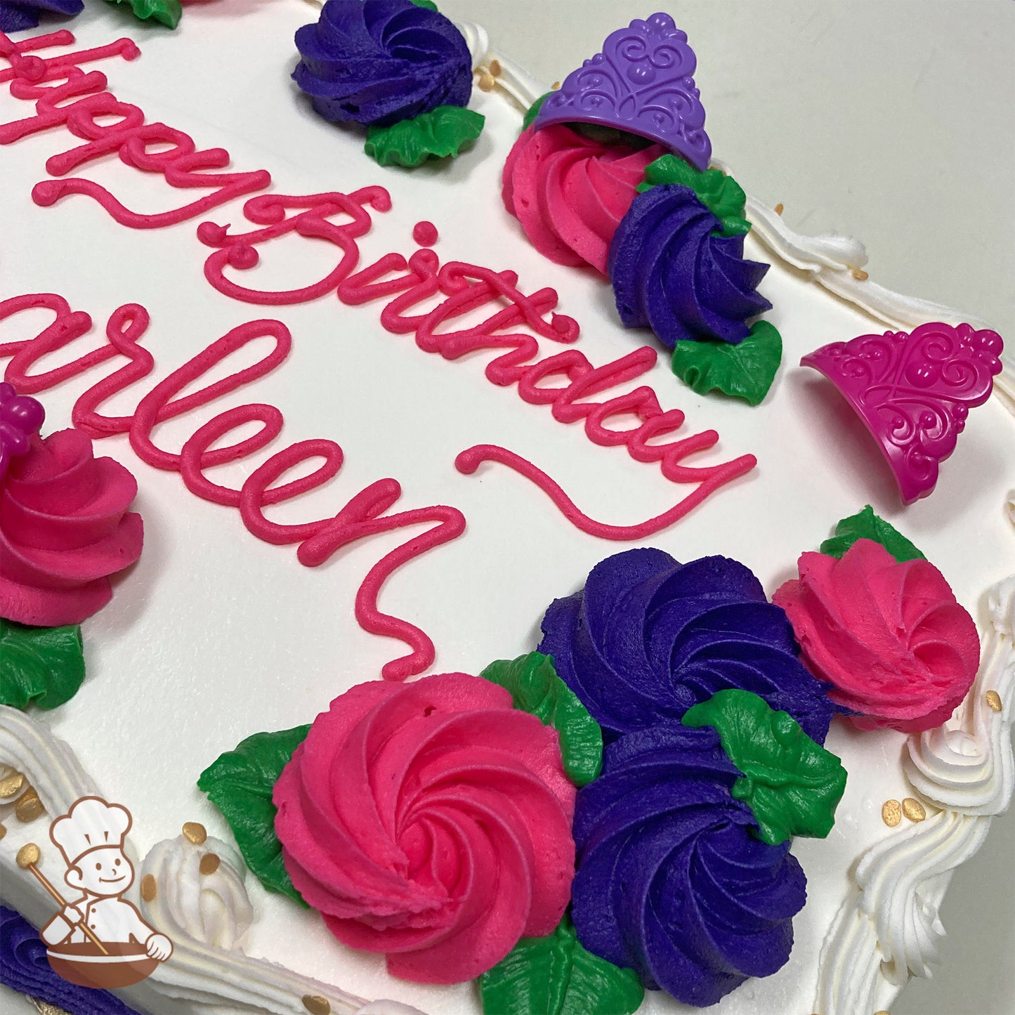 Sheet cake with pink and purple buttercream rosettes, green leaves, and plastic princess crown rings in pink and purple. White frosting border.
