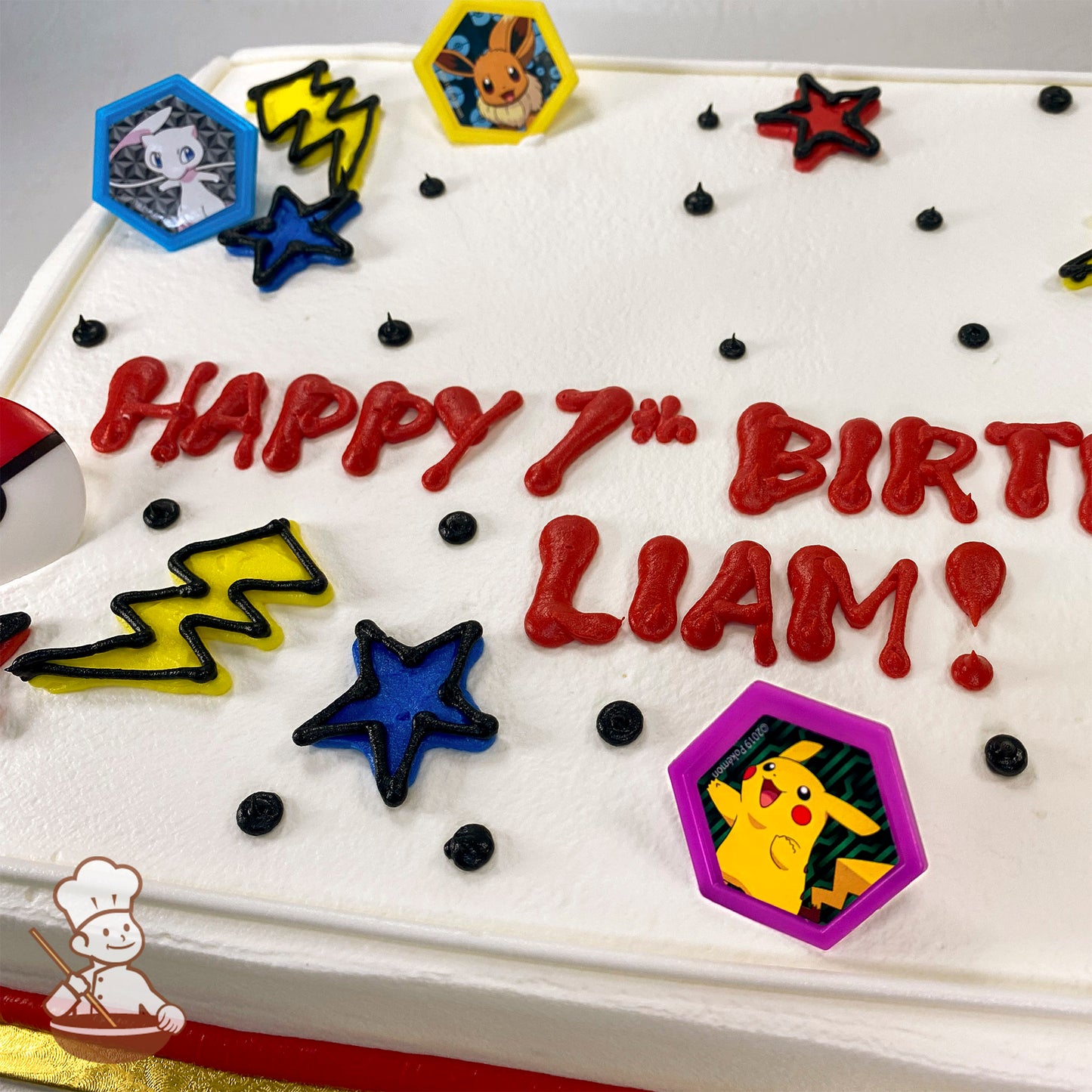Sheet cake with white icing, decorated with plastic Pokémon rings featuring Pikachu, Eevee, and Mew. Yellow lightning bolts, blue and red stars, and black dots accent the design.