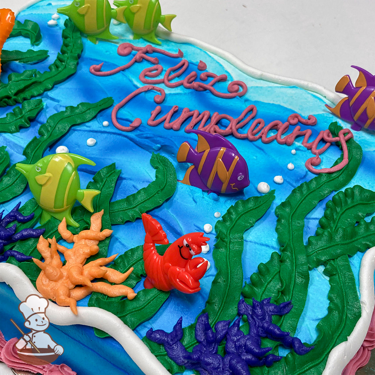Sheet cake with blue buttercream ocean, green kelp, and plastic sea life rings including fish and a red lobster. Orange coral accents.