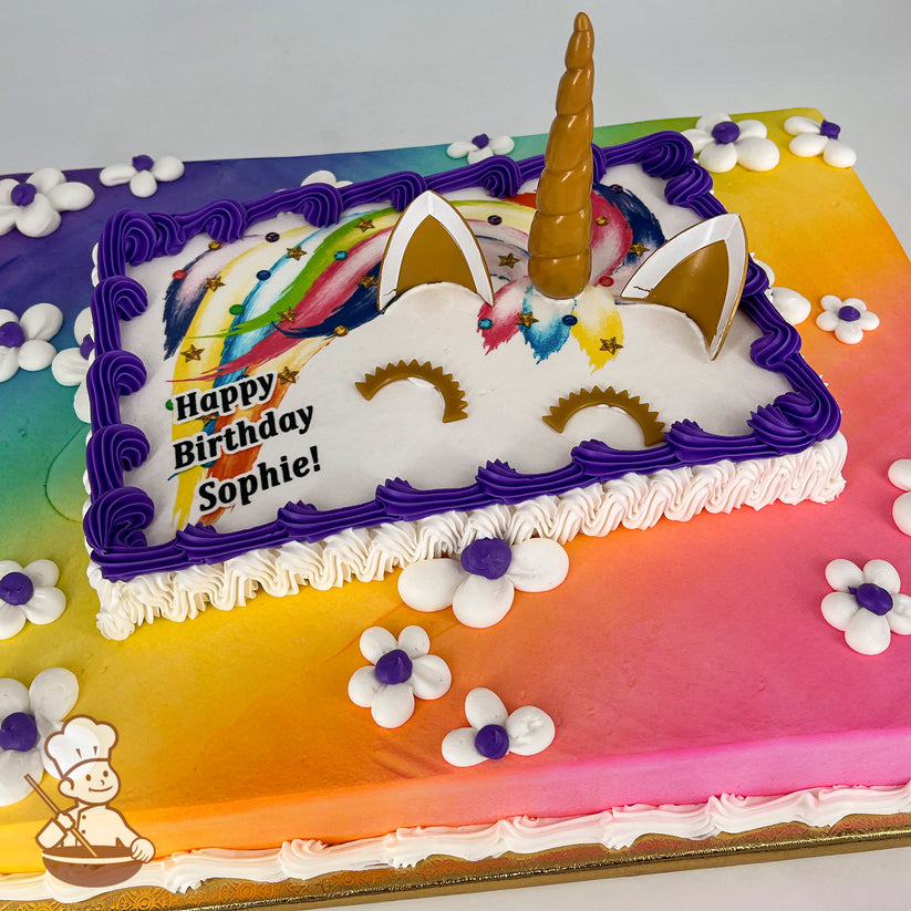 Sheet cake with a rainbow gradient background, decorated with a unicorn face featuring a golden horn, ears, and closed eyes. Purple buttercream borders and white daisies with purple centers adorn the cake.