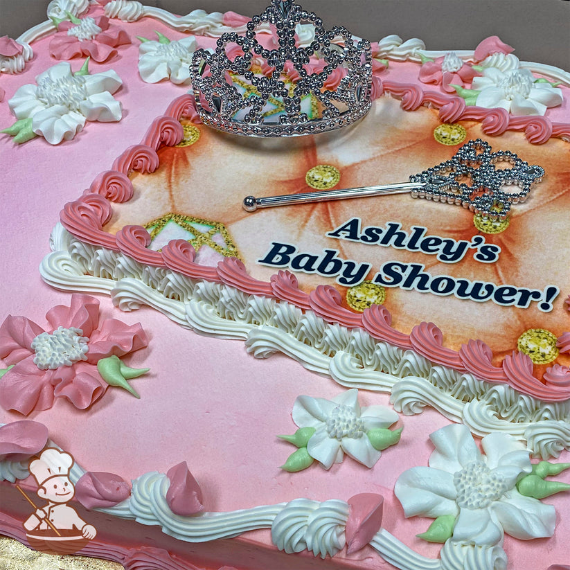 Sheet cake with pink and white Hawaiian buttercream flowers, a plastic crown, and scepter toy set on top.
