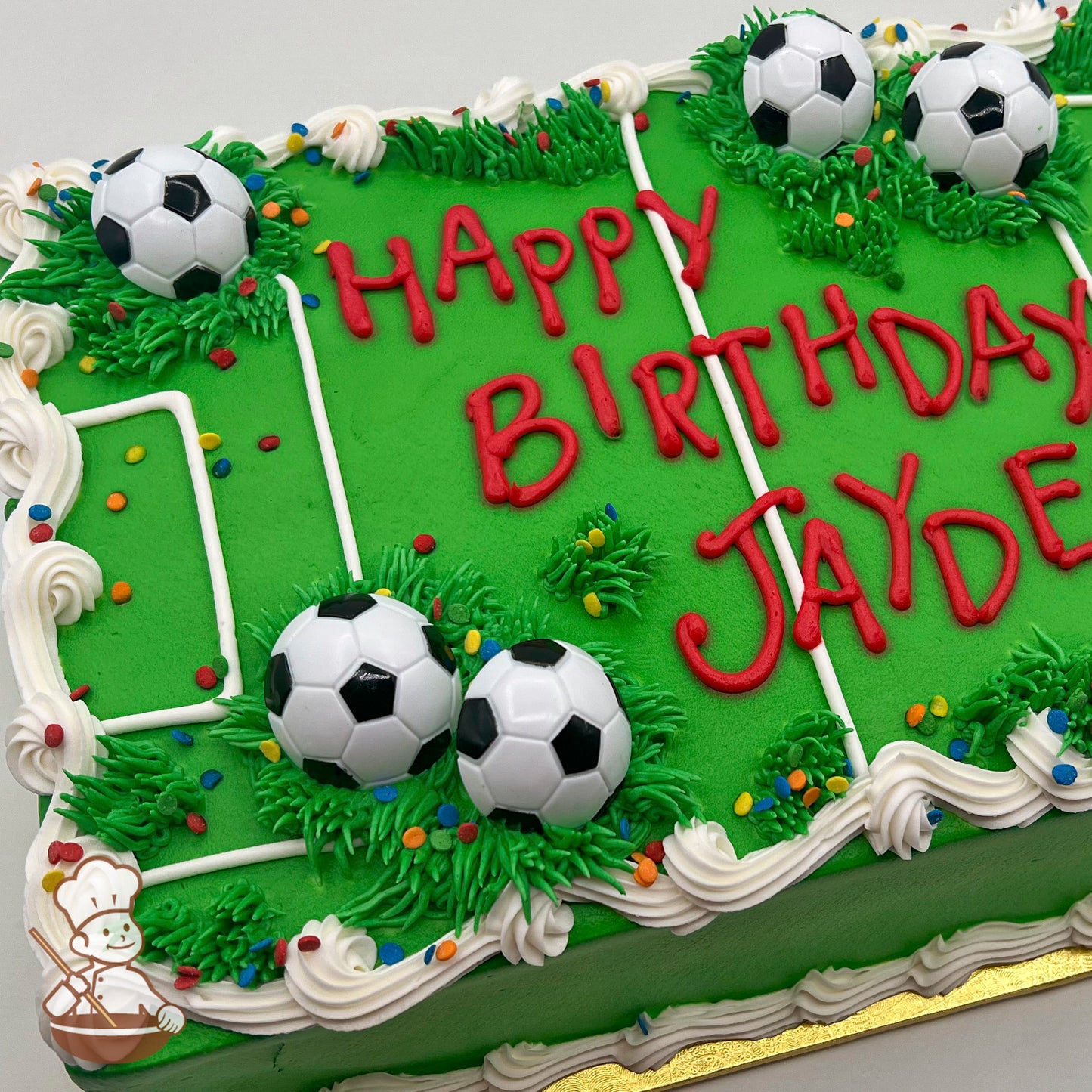 A rectangular sheet cake decorated as a soccer field with green buttercream grass, white field lines, plastic soccer ball toppers, and colorful sprinkles.