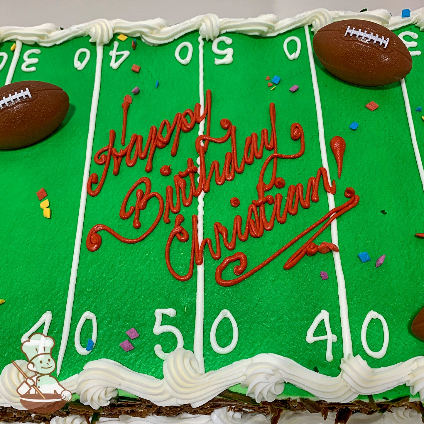 Sheet cake decorated as a football field with green icing, white yard lines, and plastic football toy rings. Colorful sprinkles scattered on top.