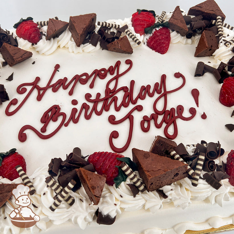 Sheet cake with white frosting, decorated with strawberries, brownie triangles, chocolate curls, and striped chocolate sticks along the edges.